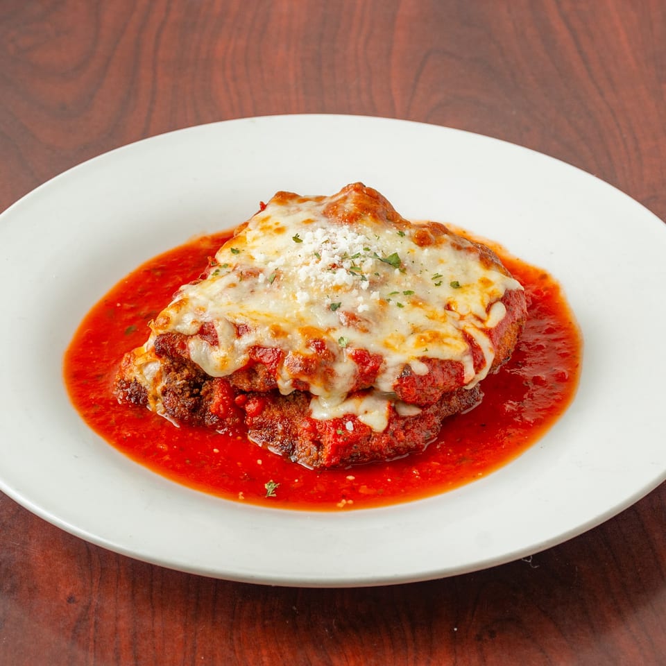 Chicken parmesan with melted mozzarella, marinara sauce, and parsley on a white plate.
