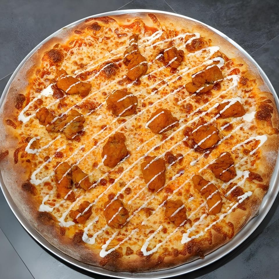 A Familia Pizzeria buffalo chicken pizza, drizzled with white sauce, on a metal tray.