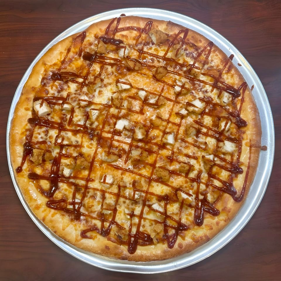 A Familia Pizzeria BBQ chicken pizza with cheese and sauce drizzle on a metal pan.