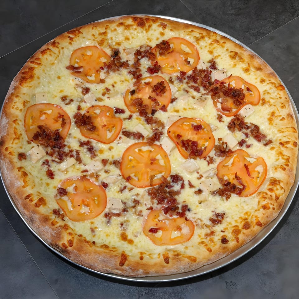 Familia Pizzeria's white pizza with melted cheese, sliced tomatoes, and crumbled bacon.